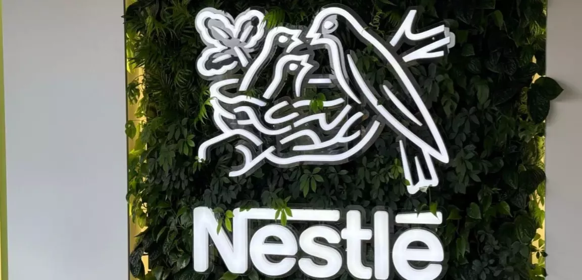 Illuminated Nestlé logo with birds and a nest, mounted on a green plant wall with vertical light panels on both sides.
