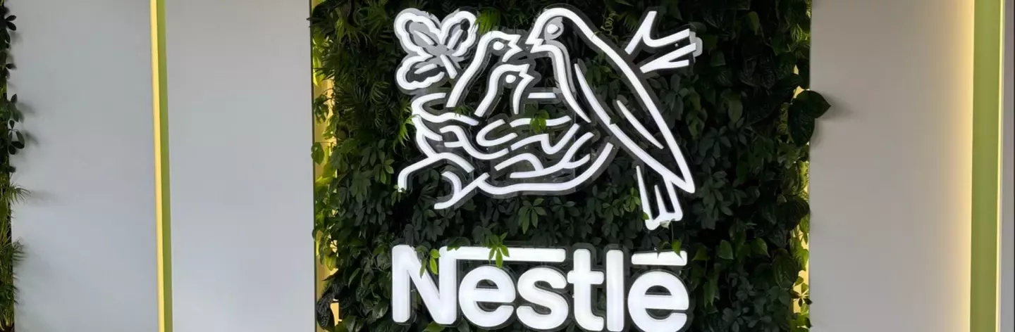 Illuminated Nestlé logo with birds and a nest, mounted on a green plant wall with vertical light panels on both sides.