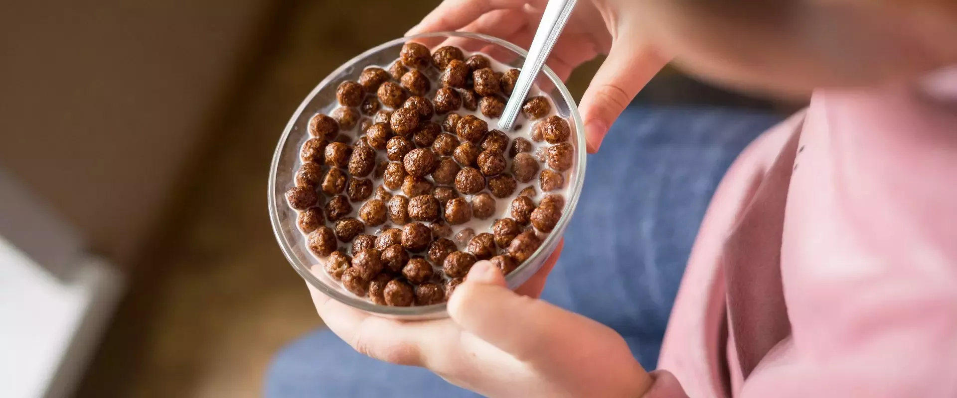 A child holds a bowl of chocolate cereal in milk, ready to eat, with a spoon resting on the edge, hinting at delightful breakfast moments
