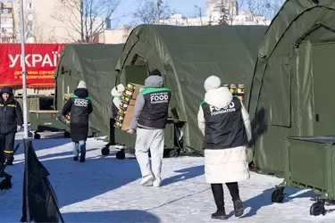 Volunteers from the Ukrainian Food Foundation carrying boxes near green tents in a snowy outdoor relief distribution area.