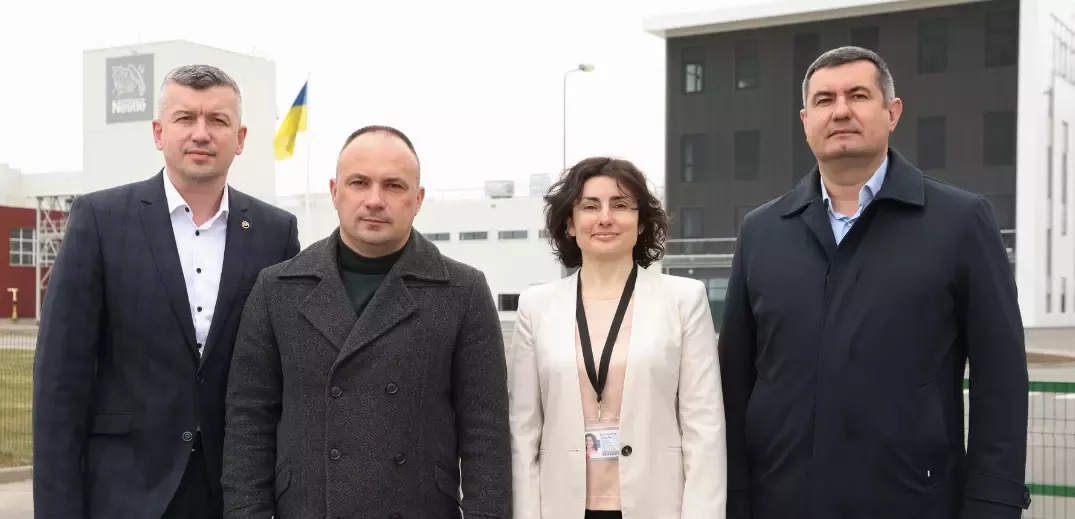 Four people in business attire standing outside near a Nestlé building with a Ukrainian flag visible in the background.